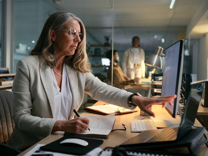 Computer, night and writing with business woman in office for budget or finance information. Accounting, bookkeeping and reading with mature employee in workplace for online financial reporting