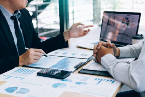 Male manager is explaining about the company's cost graph on the laptop computer for employees to listen to and share the analysis together.